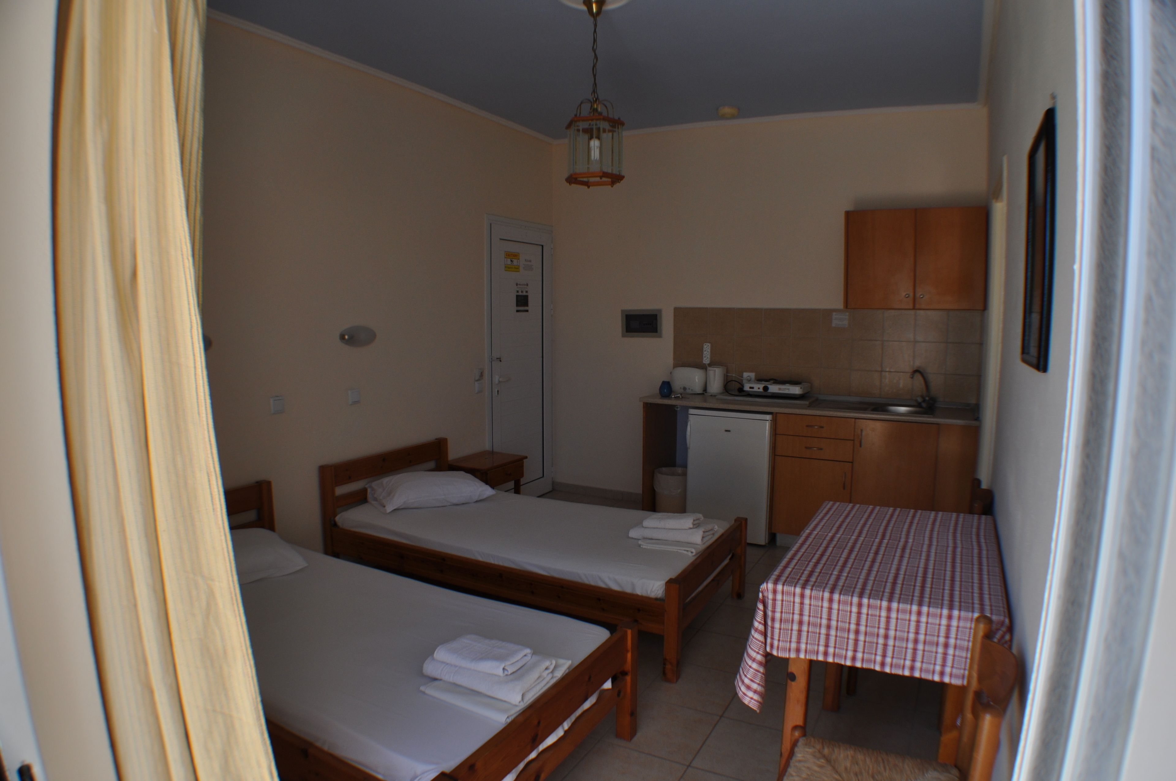 A small, compact room with two single beds, a kitchenette, and a dining table.