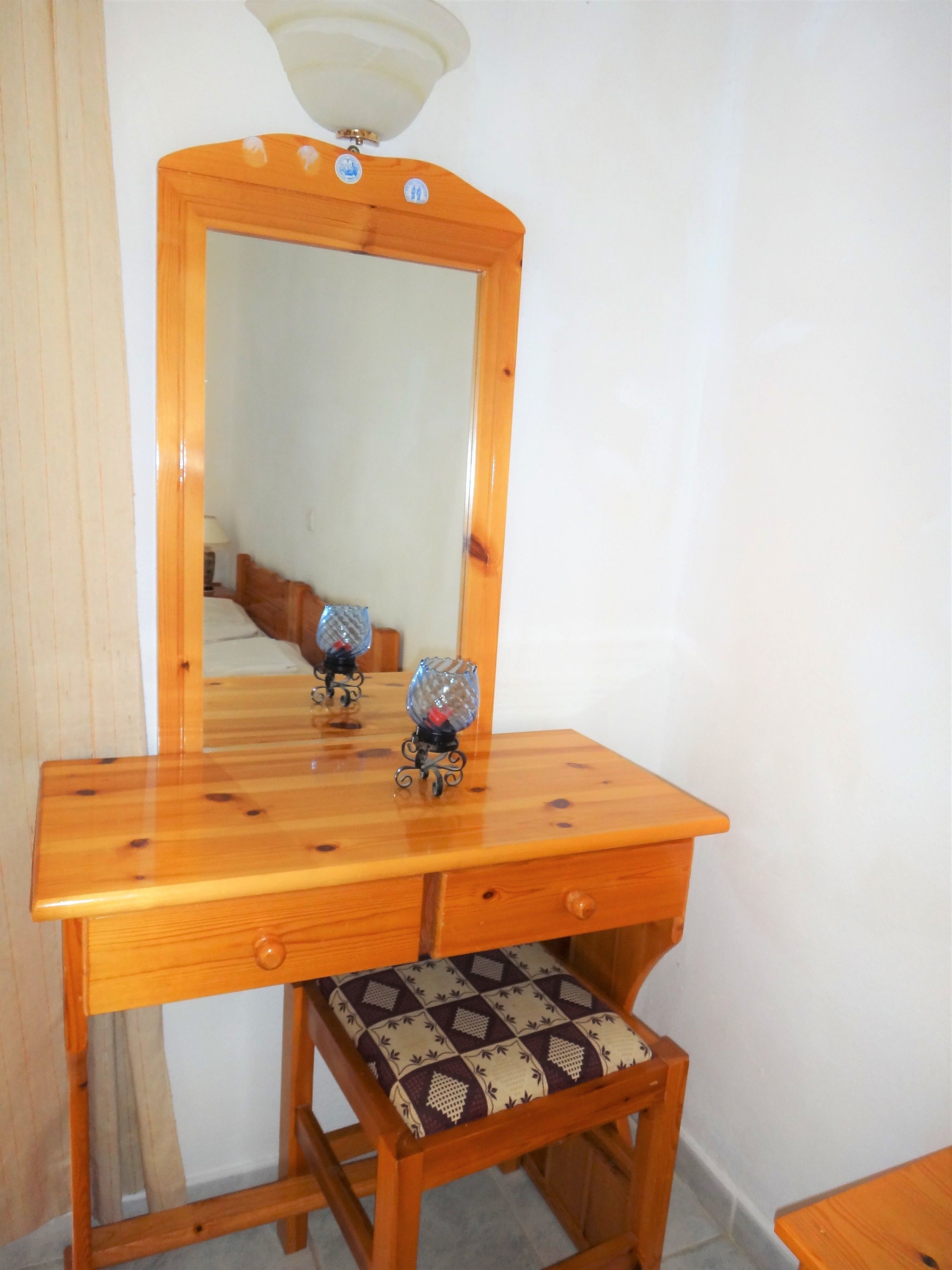 A wooden vanity with a mirror, a small stool with a patterned cushion, and a decorative glass object on the vanity.