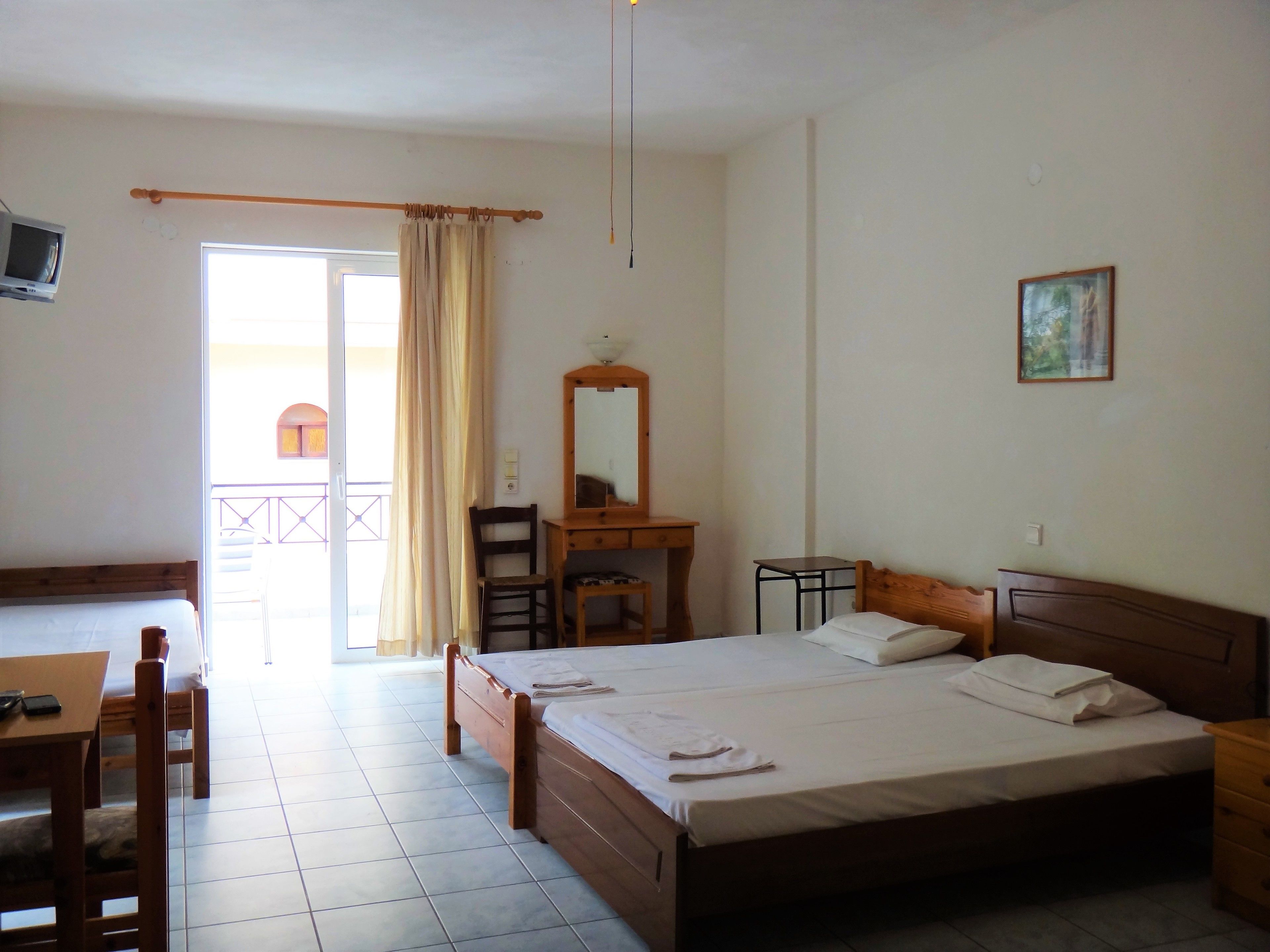 A hotel room with a bed, a desk, a chair, a small table, a mirror, and a painting on the wall.