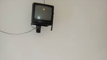 Una habitación pequeña con una mesa de madera y dos sillas, un televisor montado en la pared y un radiador en el suelo.