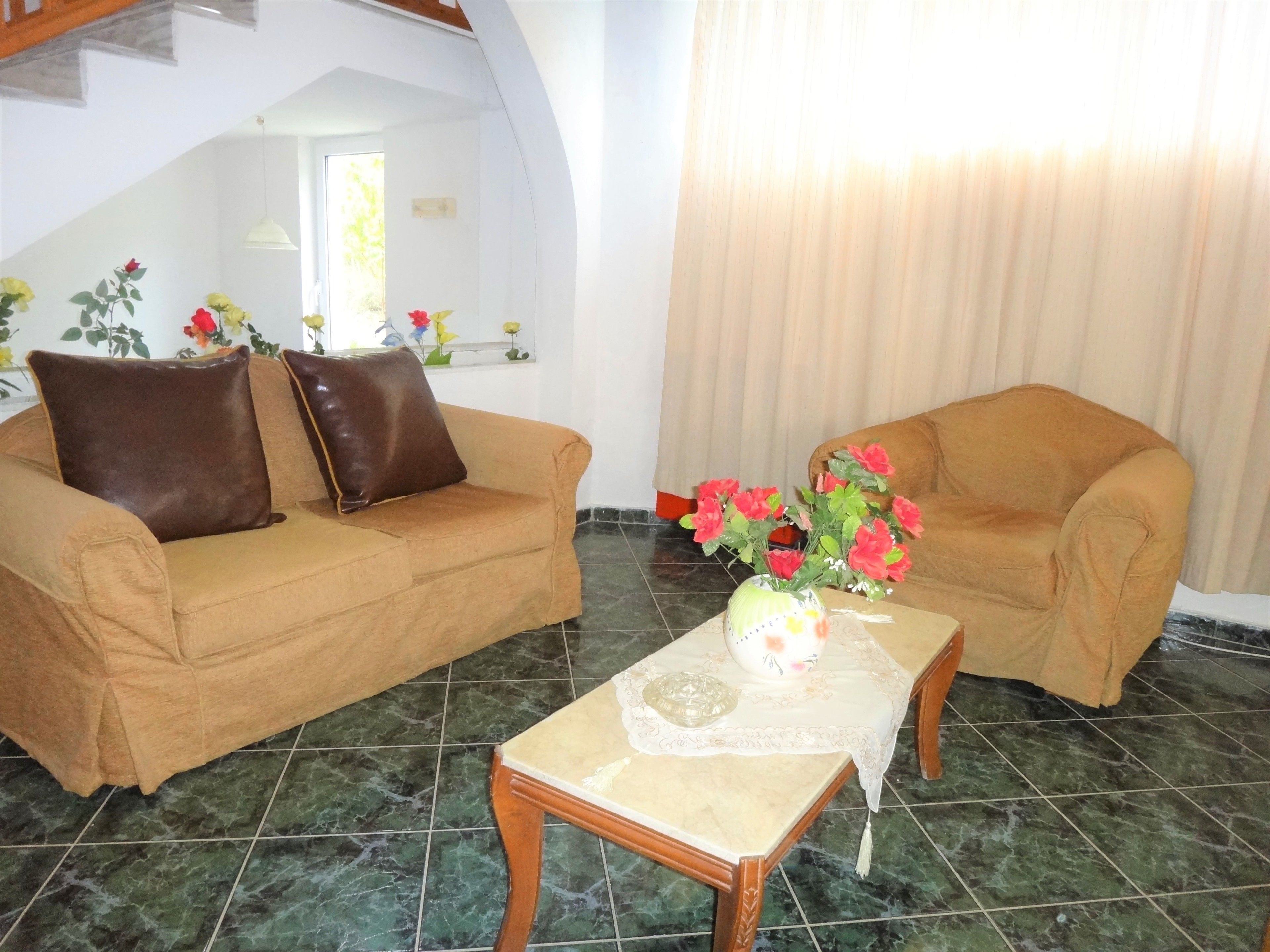 Una sala de estar con dos sofás, una mesa de centro con un jarrón de flores y vistas a una ventana con cortinas.