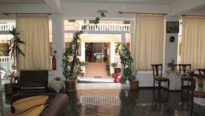 A lobby with a reception desk, seating area, potted plants, and a view of the entrance. - Pagona Hotel (Istiaia-Aidipsos)