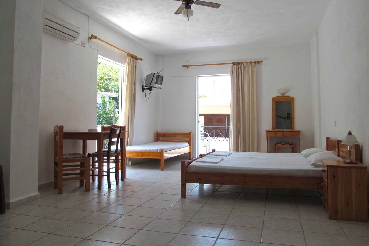 A room with a bed, a desk, a chair, a TV, and a ceiling fan.