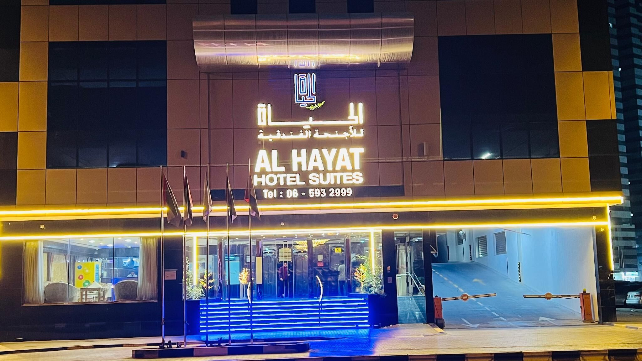 Het exterieur van Al Hayat Hotel Suites, met een modern ontwerp, toont een opvallende ingang met glazen deuren en een trap naar de entree.