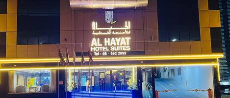 Het exterieur van Al Hayat Hotel Suites, met een modern ontwerp, toont een opvallende ingang met glazen deuren en een trap naar de entree.
