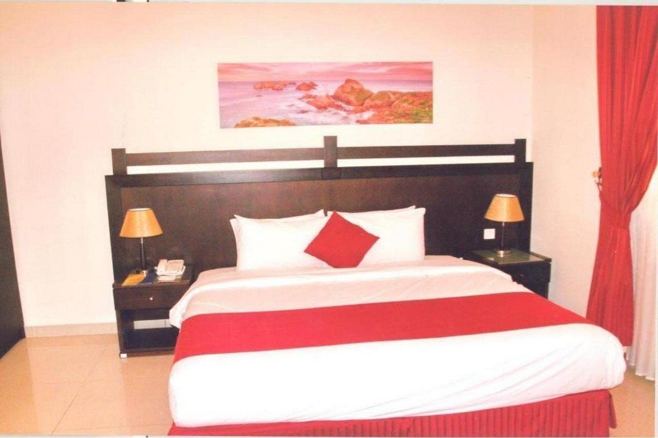 Camera d'albergo con un letto, due comodini, un tavolino e un quadro appeso al muro, con tende rosse.