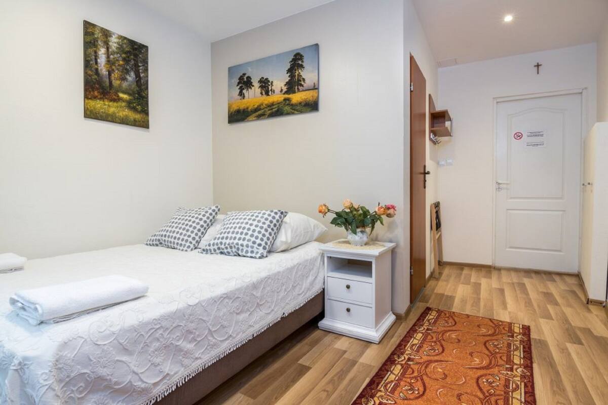 A bedroom with a bed, white nightstand, and a painting of a forest.