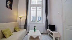 A room with a white sofa, a small table with a plant, a television on a stand, and a window with curtains. - Unikat Guest Rooms (Self-check in) (Kraków)