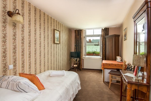 A hotel room with a bed, a desk, a chair, a television, and a window with a view of buildings.
