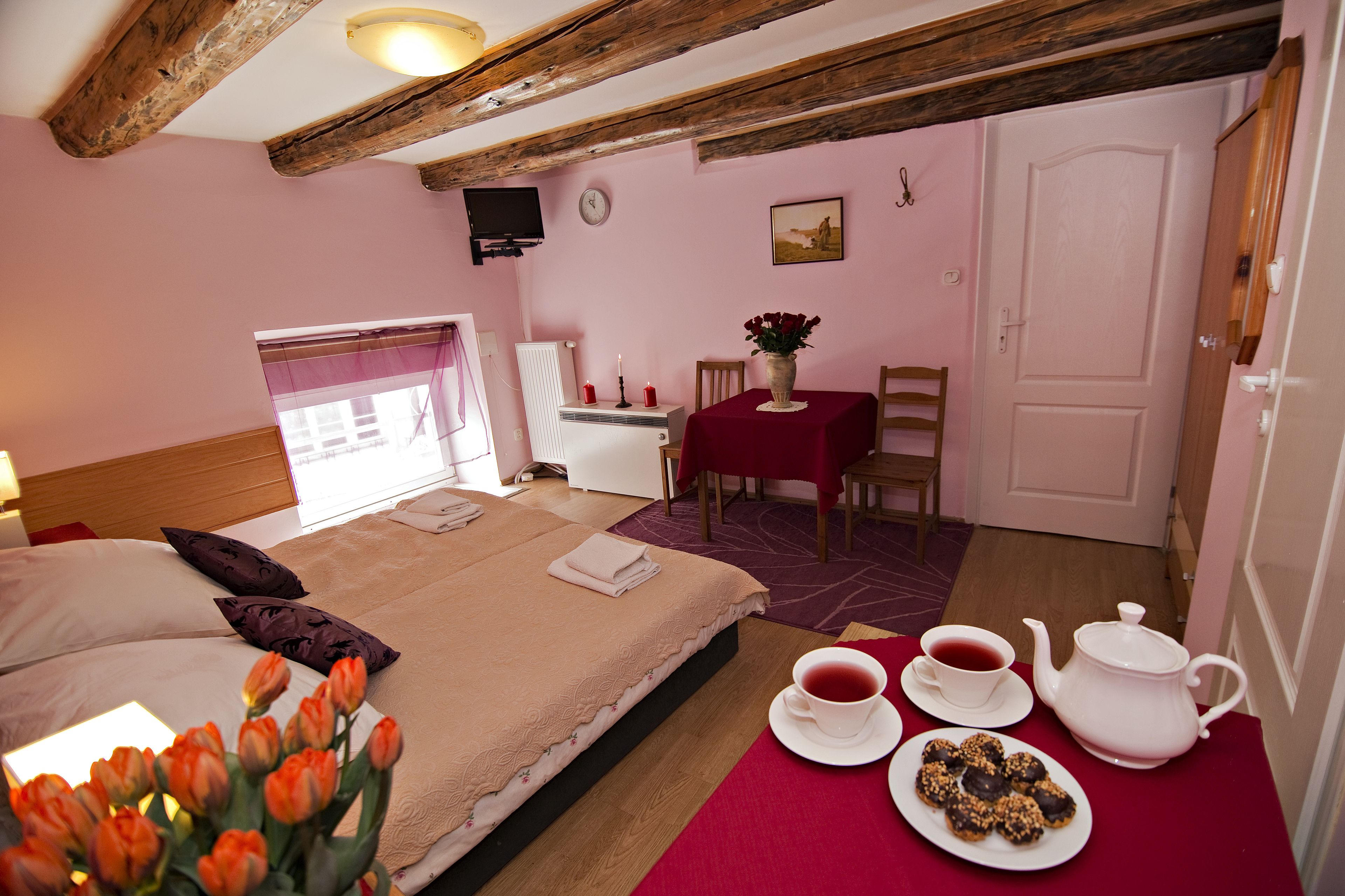 A bedroom with a bed, a table with a teapot and cups, a small table with a vase of flowers, and a chair.