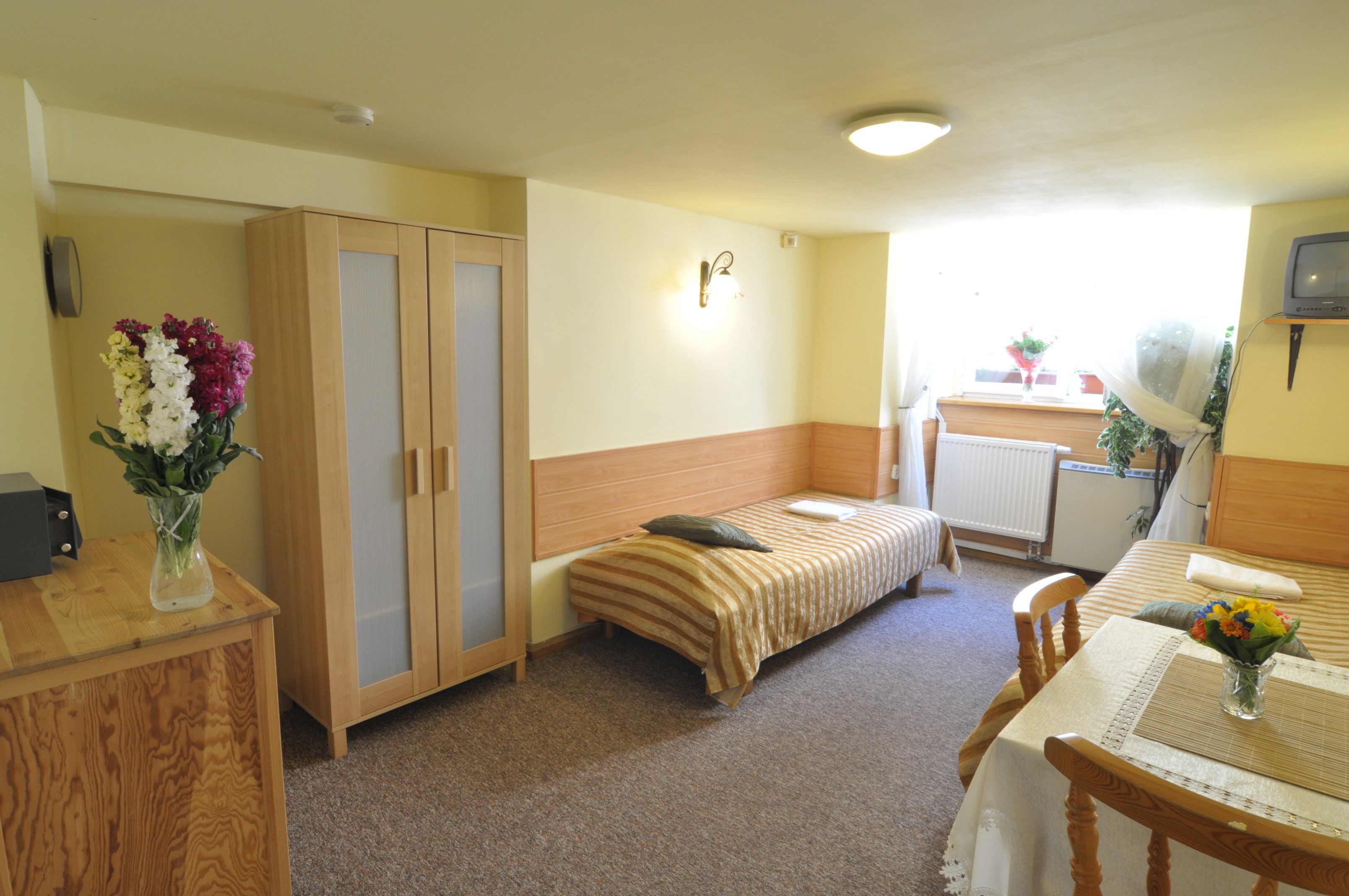 Un dormitorio con una cama individual, un armario de madera, una mesita con una silla y una ventana con vistas al exterior.