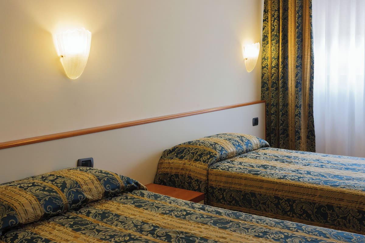A hotel room with two beds, a wooden headboard, and a nightstand.