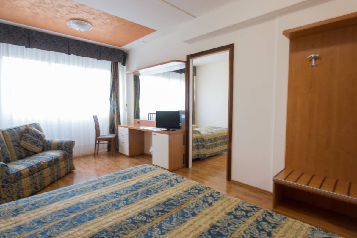 Un dormitorio con cama, escritorio, silla, armario y ventana con cortinas.