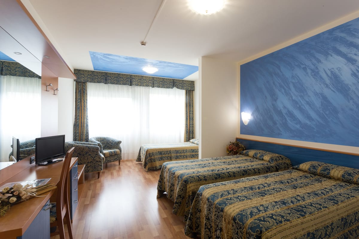 Una habitación de hotel con una cama grande, un escritorio con computadora y un ventanal con cortinas.