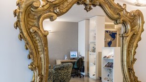 A large ornate mirror with a gold frame, reflecting a room with a desk, chair, and shelves. - Hotel Airmotel (Mestre)