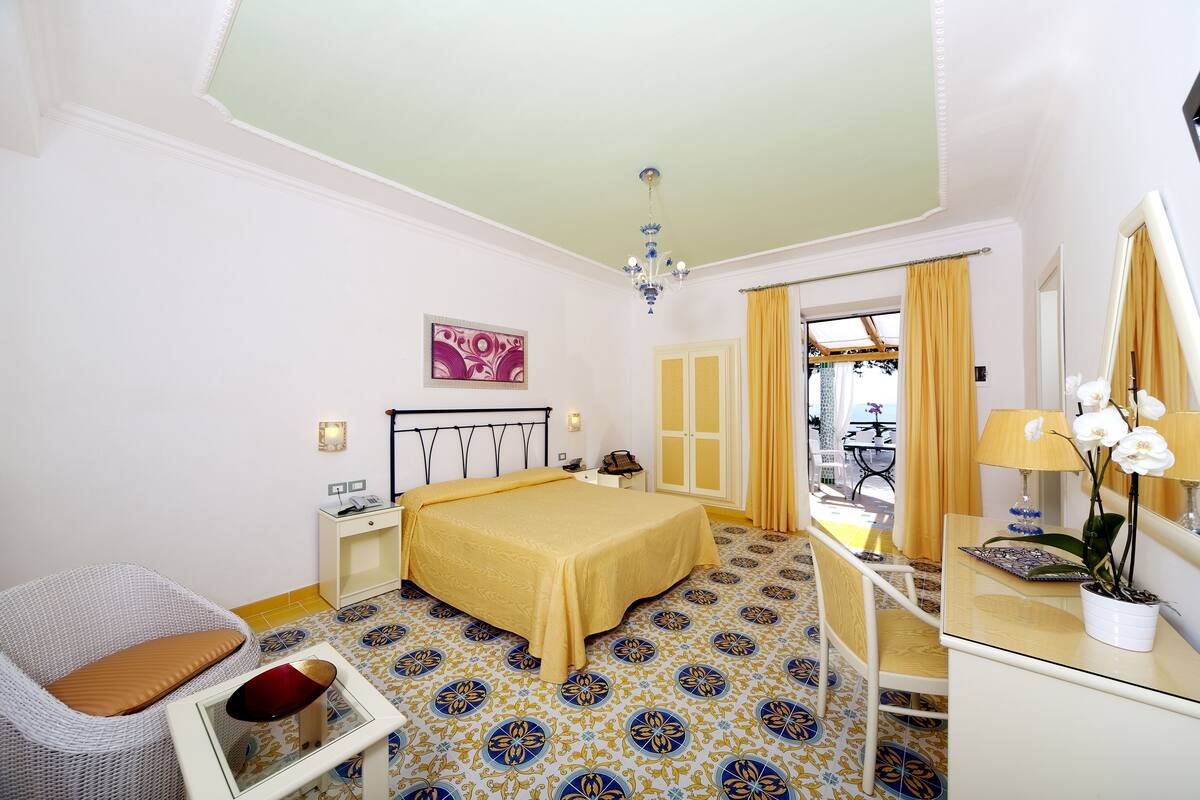 Ein Hotelzimmer mit Bett, Stuhl, Schreibtisch, Spiegel und einer Zimmerpflanze.