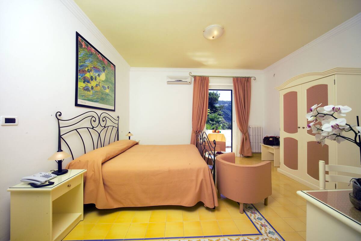 Ein Schlafzimmer mit Bett, Nachttisch, Lampe und Blick ins Freie.