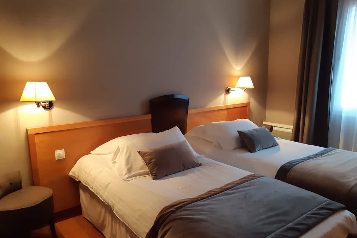 Une chambre d’hôtel avec deux lits, chacun doté d’une tête de lit, d’une table de chevet et d’une lampe.