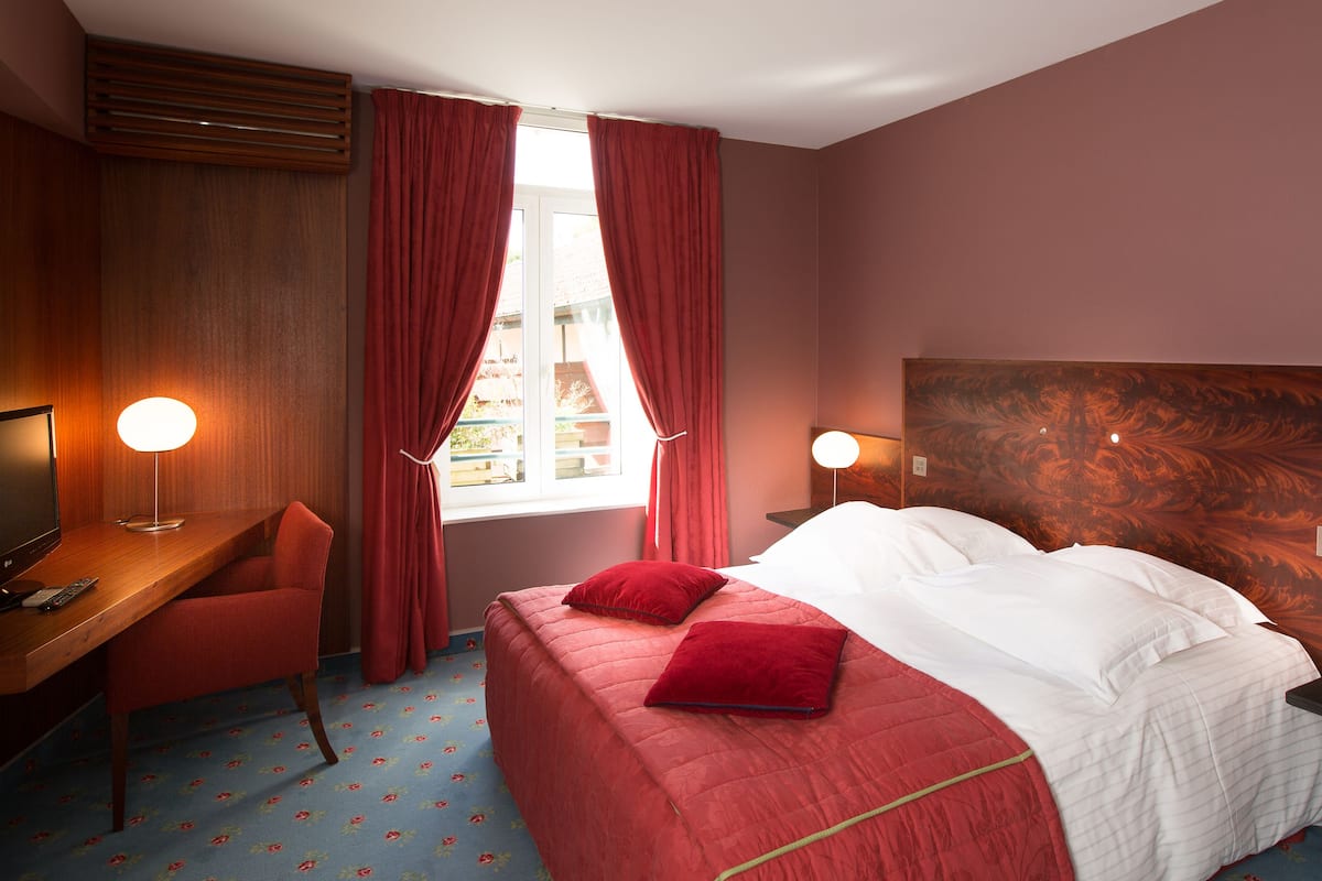 Une chambre d’hôtel avec un lit, un bureau, une chaise et une fenêtre avec des rideaux.