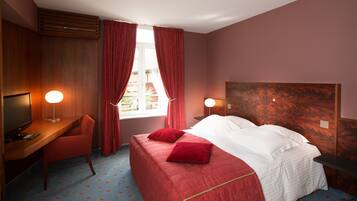 A hotel room with a bed, a desk, a chair, and a window with curtains.