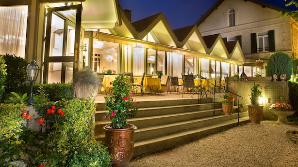 Een hotel met een overdekt terras, een trap naar de ingang en plantenpotten.