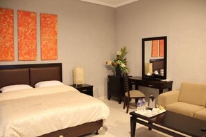 A hotel room with a large bed, a desk with a chair, a sofa, and a mirror. - The Radiant Villa's & Function Hall (Lembang)