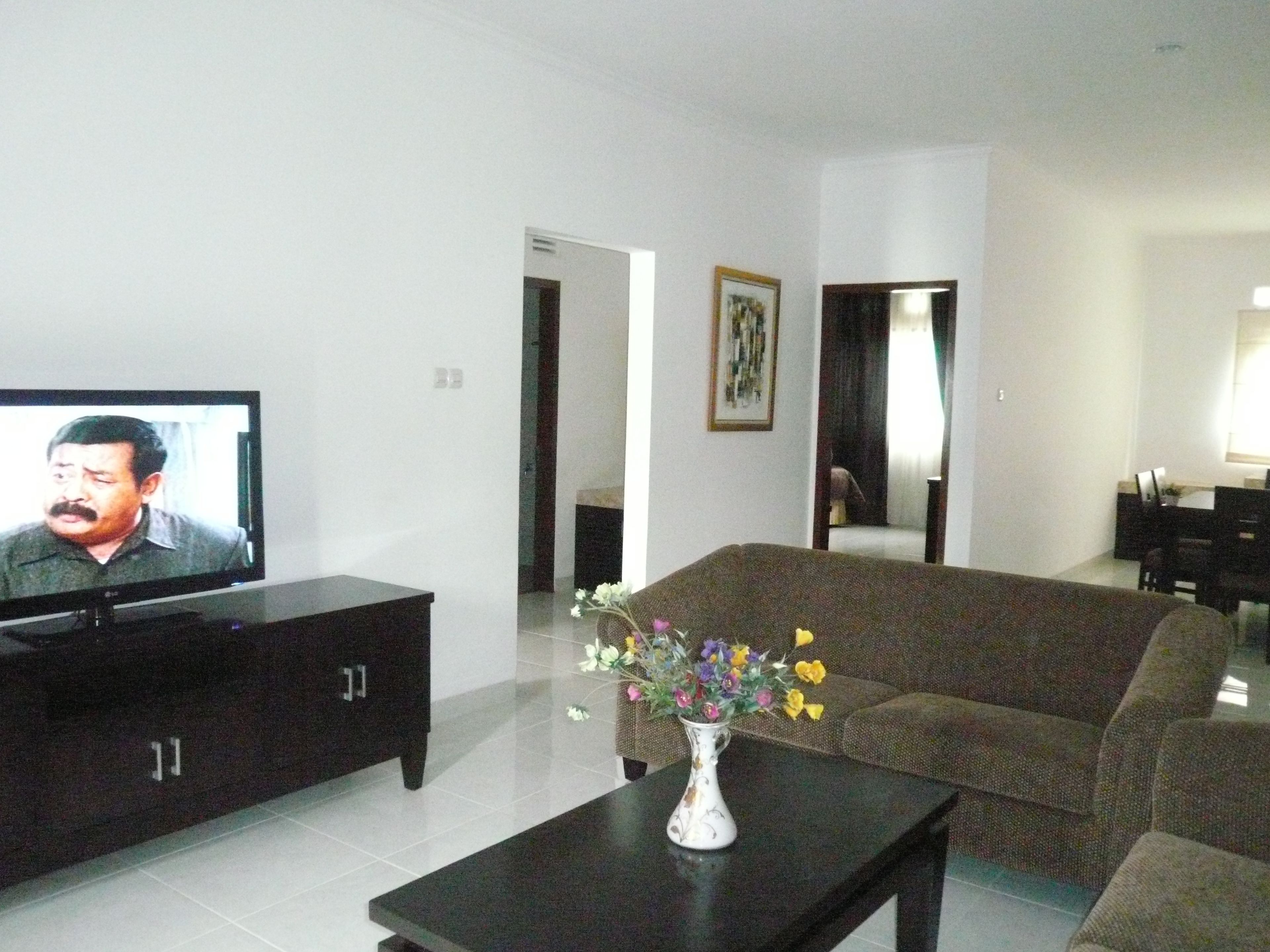 Ein Wohnzimmer mit Fernseher, einer Couch, einem Couchtisch und einer Vase mit Blumen.