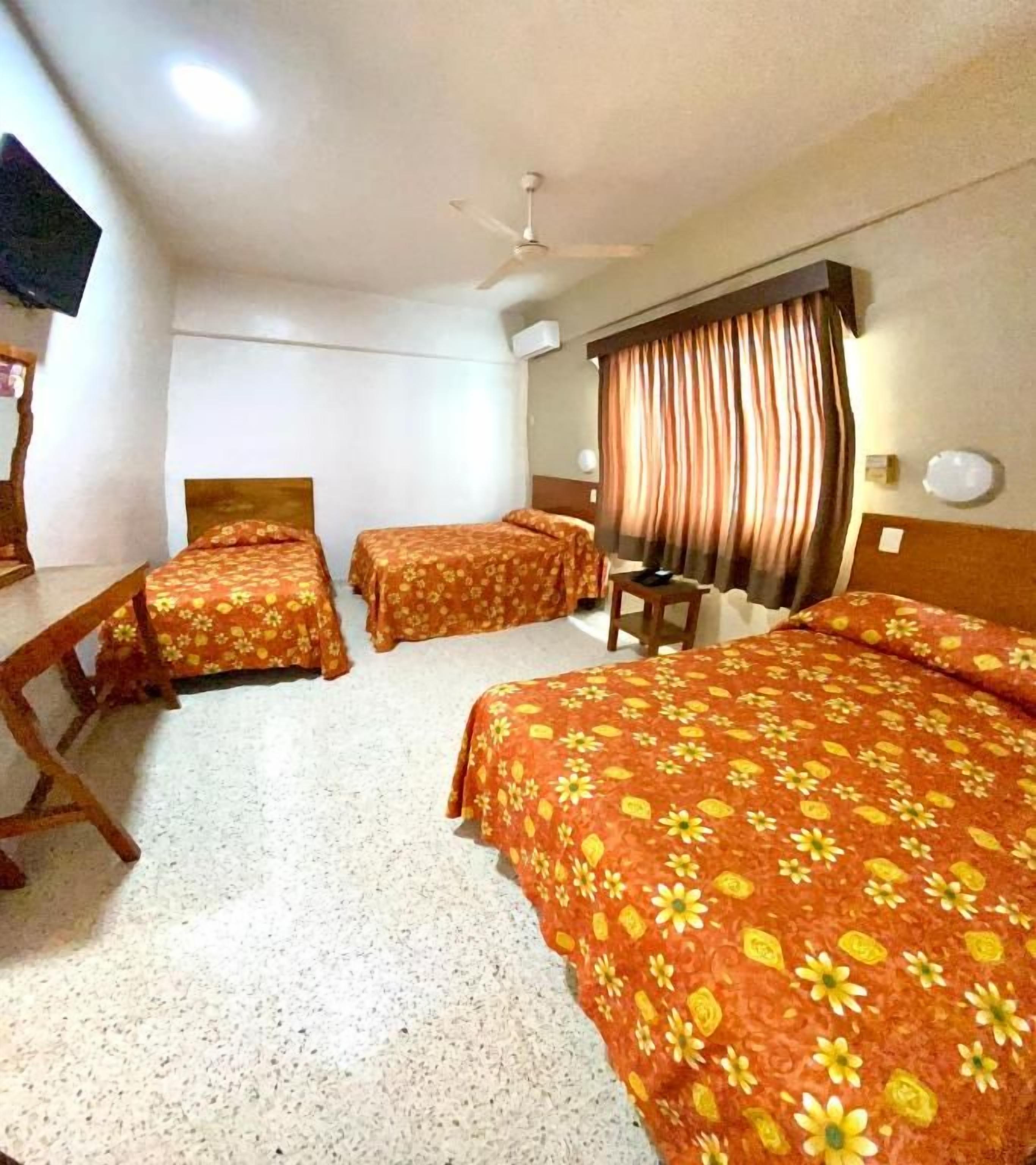 A hotel room with two single beds, a double bed, a desk, a chair, a television, and a ceiling fan.