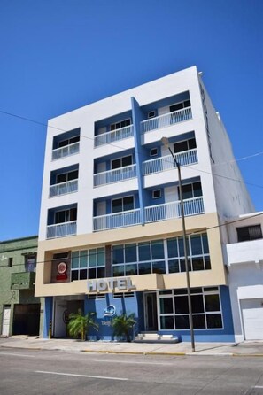 Un hôtel à plusieurs étages, doté d’une façade sobre, de balcons à chaque étage et surplombant un ciel dégagé.
