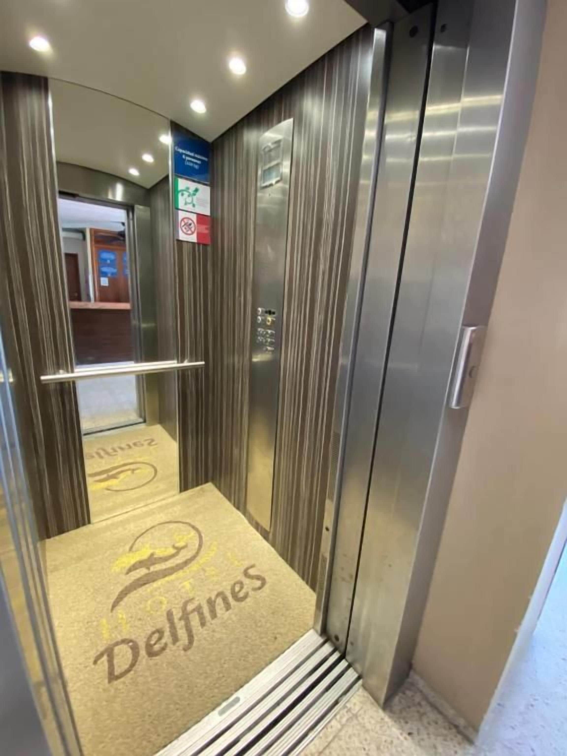 An elevator with a metallic finish, a handrail, and a carpet with the logo 'Delfines'.