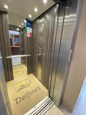 An elevator with a metallic finish, a handrail, and a carpet with the logo 'Delfines'. - Hotel Delfines (Veracruz)