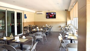 A cafe with tables and chairs, a TV mounted on the wall, and a sign indicating the exit. - Hotel Delfines (Veracruz)