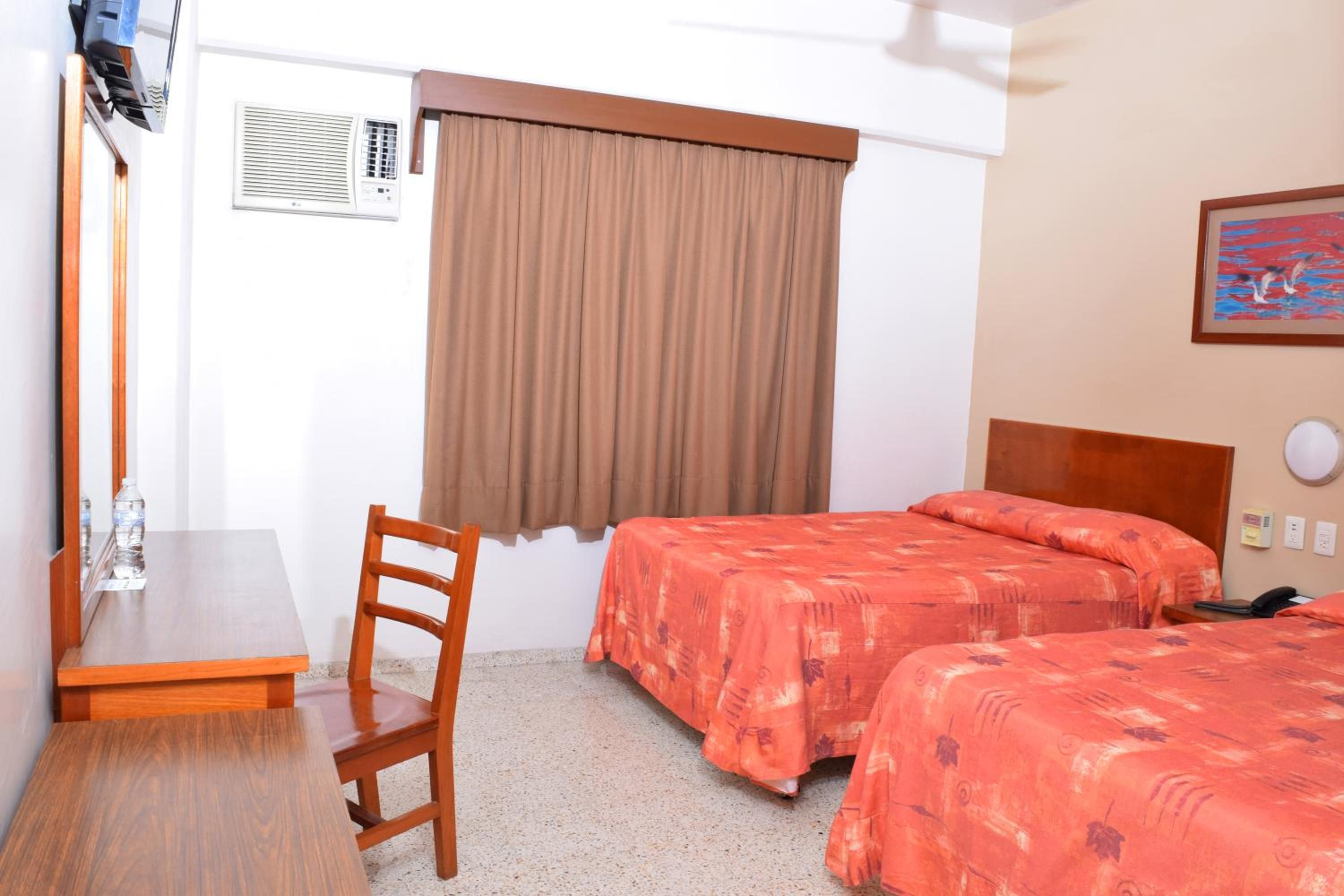 Habitación de hotel con dos camas, un escritorio, una silla, una ventana con cortinas y un cuadro en la pared.