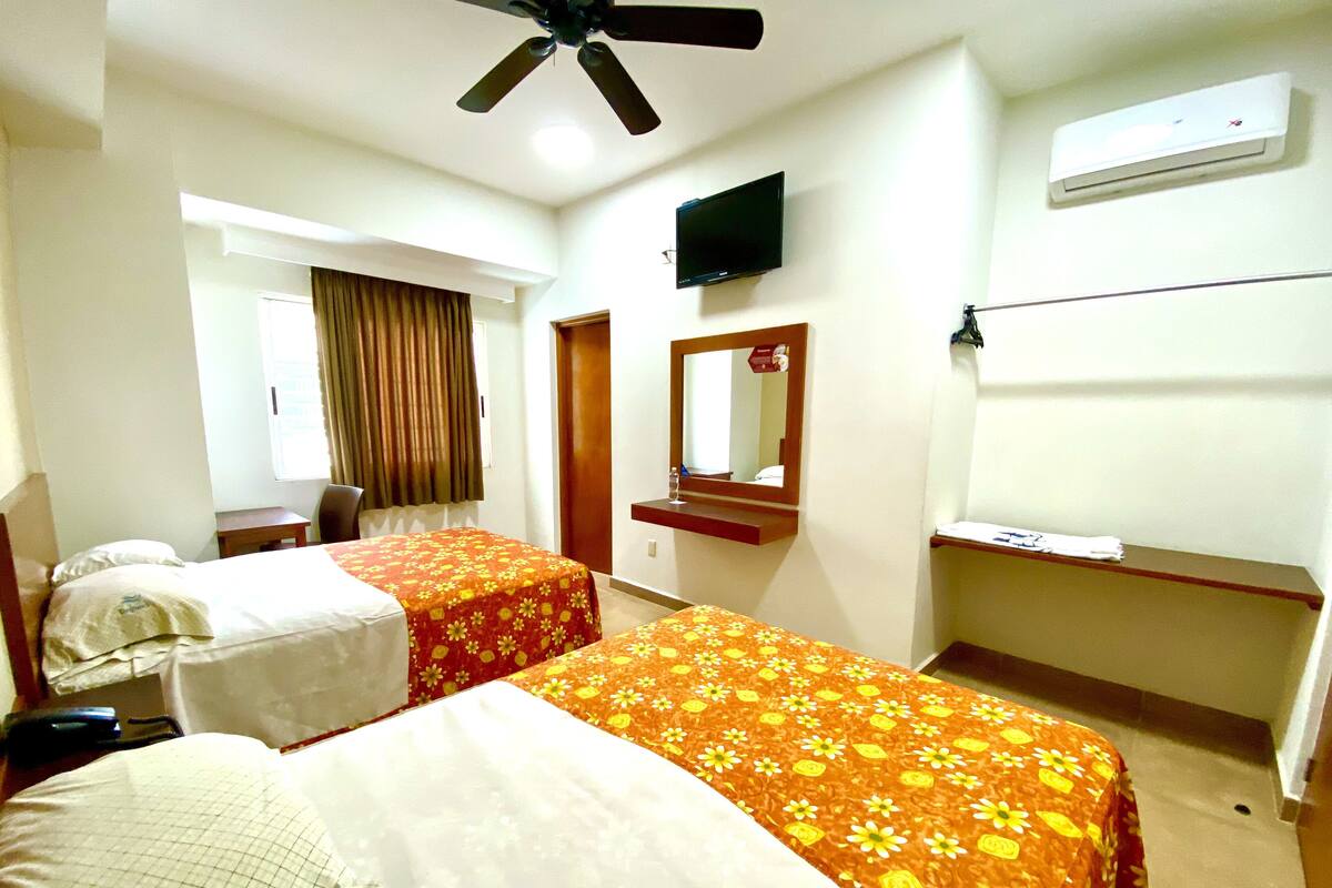 A hotel room with two beds, a ceiling fan, a TV, and an air conditioning unit.