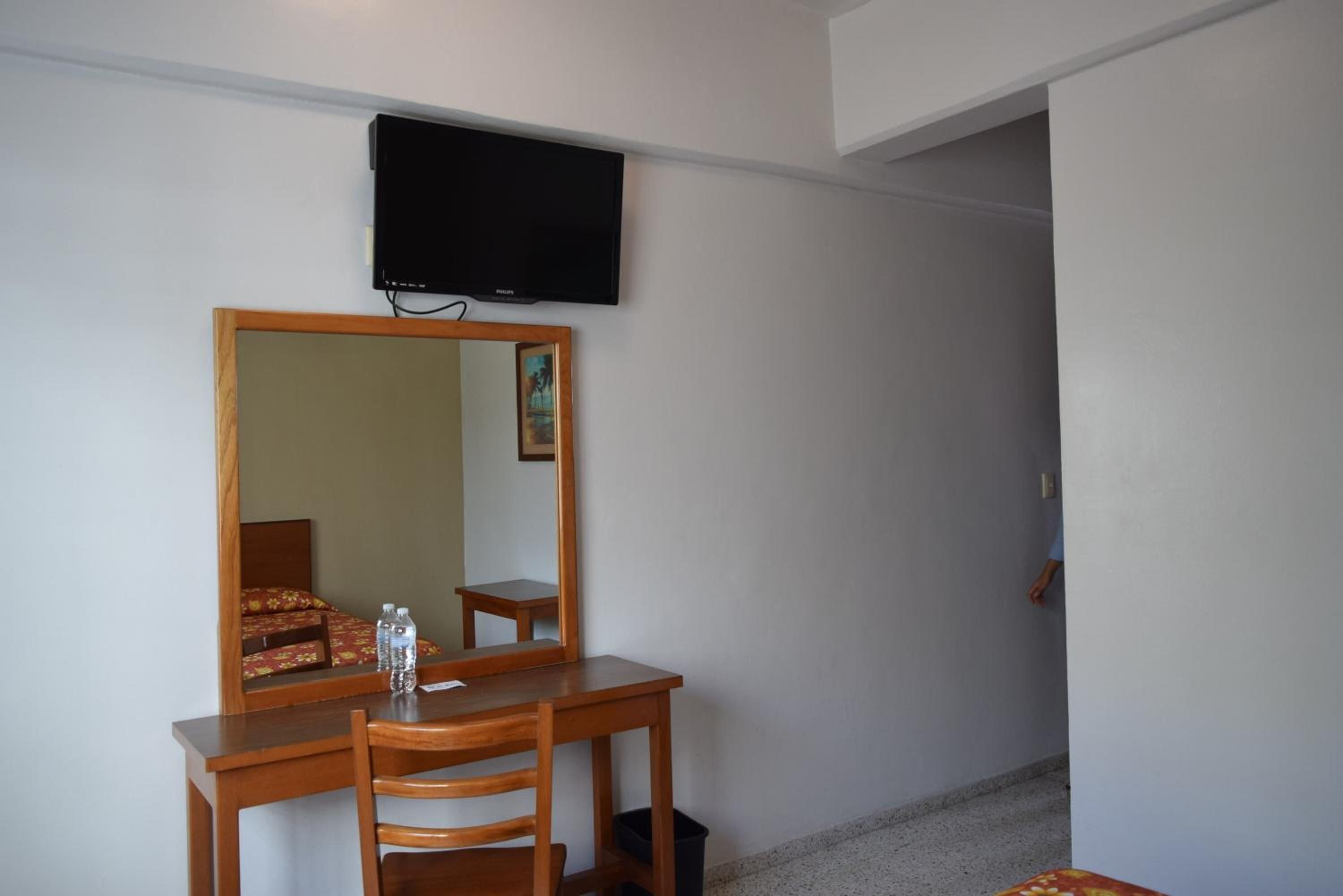 Ein Hotelzimmer mit einem Holztisch, einem Stuhl, einem flachbildfernseher an der Wand und einem kleinen Tisch mit zwei Wasserflaschen.