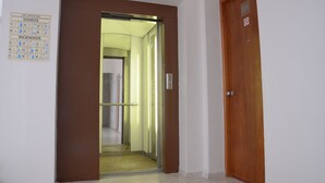 An interior hallway with a brown door and a glass elevator door. - Hotel Delfines (Veracruz)