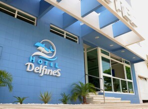 Entrada de un hotel con fachada azul, un logotipo de delfín y el nombre 'Hotel Delfines'.