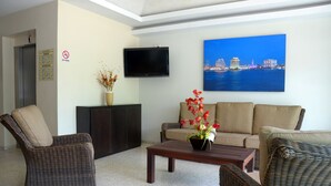 A living room with wicker furniture, a flat-screen TV, a painting of a cityscape, and a sign indicating no smoking. - Hotel Delfines (Veracruz)