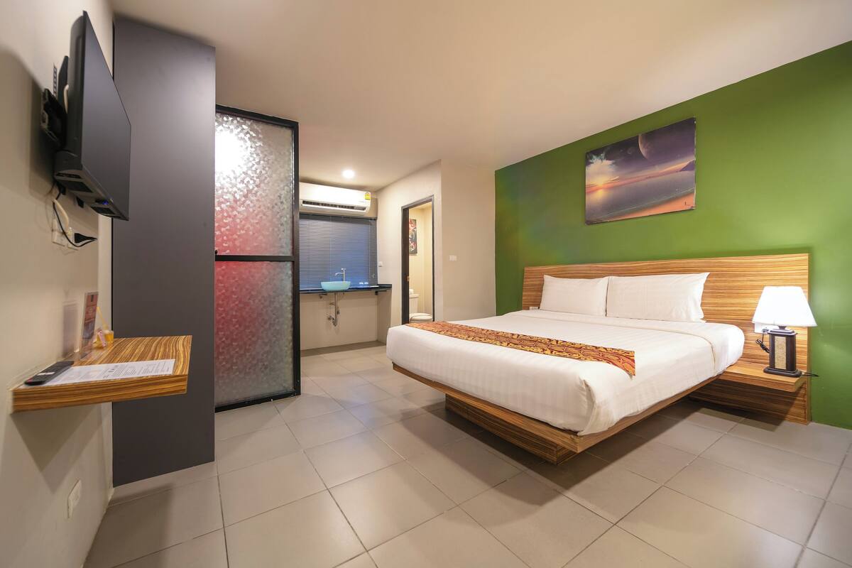 A hotel room with a bed, a TV mounted on the wall, a wooden nightstand, and a green wall.