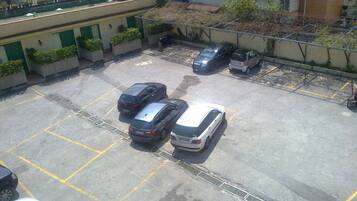 Eine Vogelperspektive auf einen Parkplatz mit mehreren Autos, ein Gebäude mit grünen Fensterläden und ein eingezäunter Bereich mit Pflanzen.