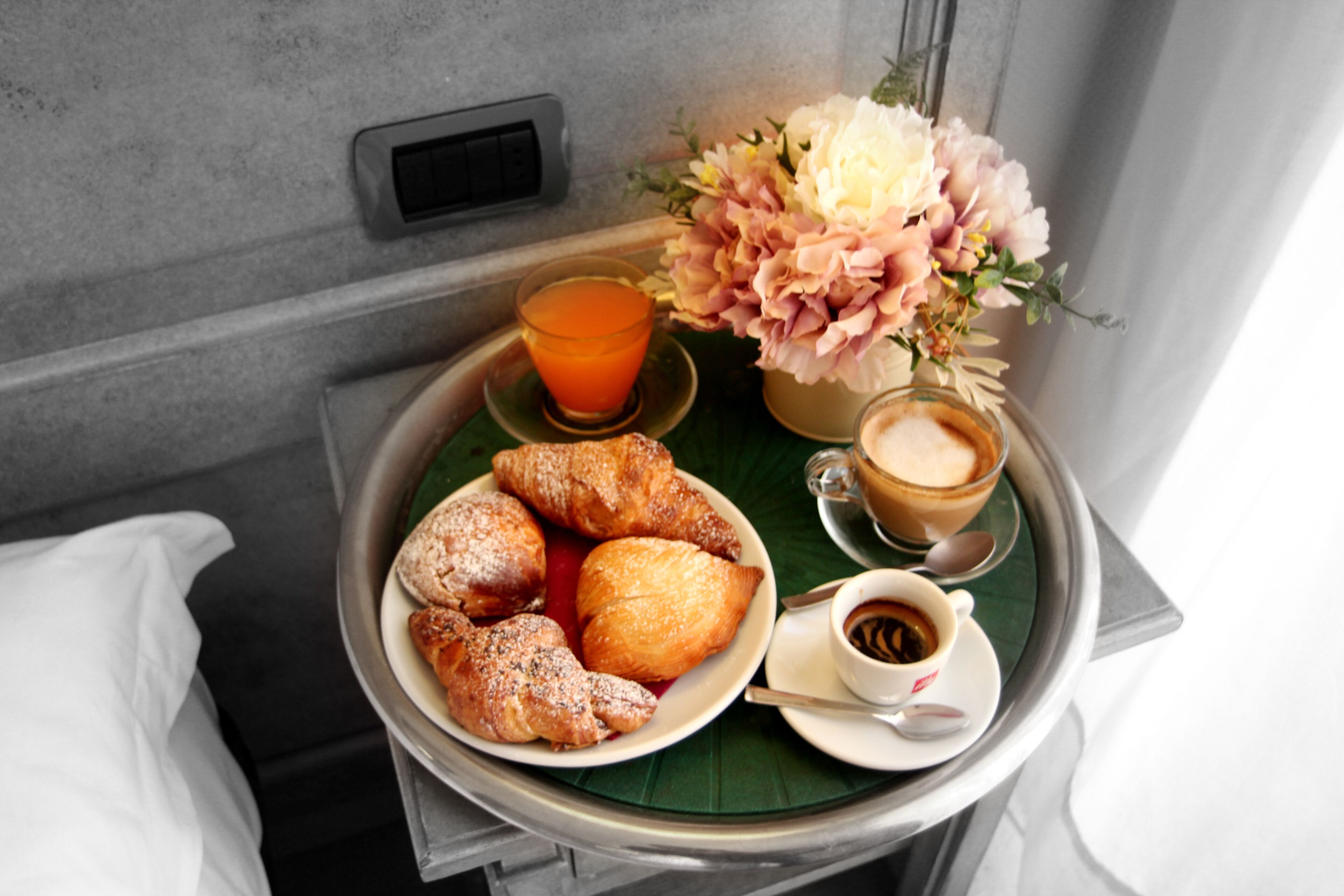 Een ontbijfwagen met croissants, een glas sinaasappelsap, een kop koffie en een vaas bloemen.