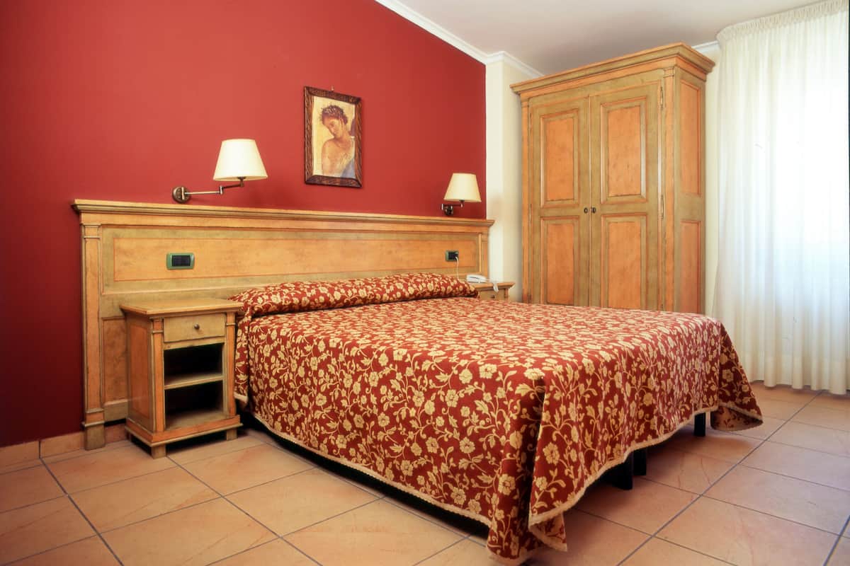 Ein Schlafzimmer mit einem Bett, einer hölzernen Kommode, einem Nachttisch, einer Lampe und einem gerahmten Bild an der Wand.