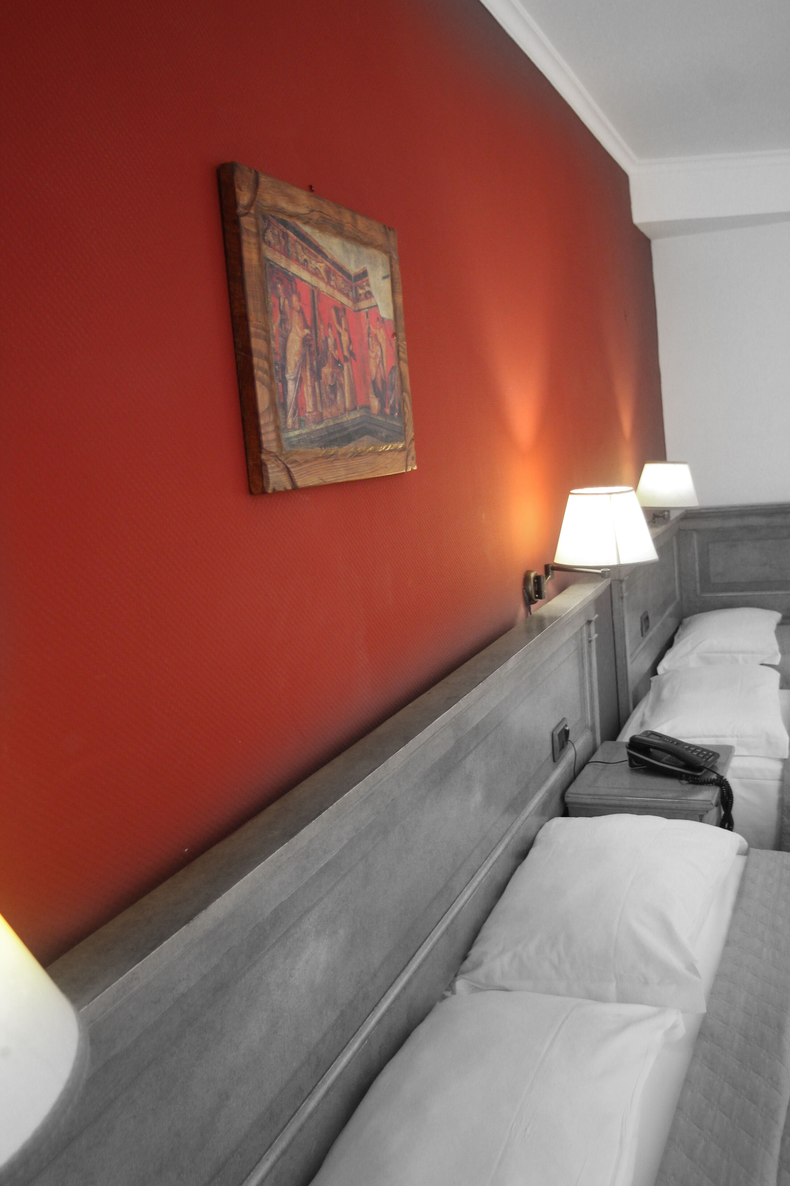 A hotel room with a red wall, a painting, two bedside lamps, and a bed with white linens.