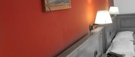 A hotel room with a red wall, a painting, two bedside lamps, and a bed with white linens.
