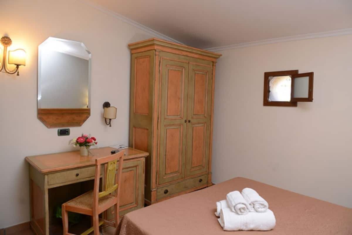 Ein Schlafzimmer mit einem Bett, einem Holztisch mit Stuhl, einem Kleiderschrank, einem Spiegel und einer Wandleuchte.