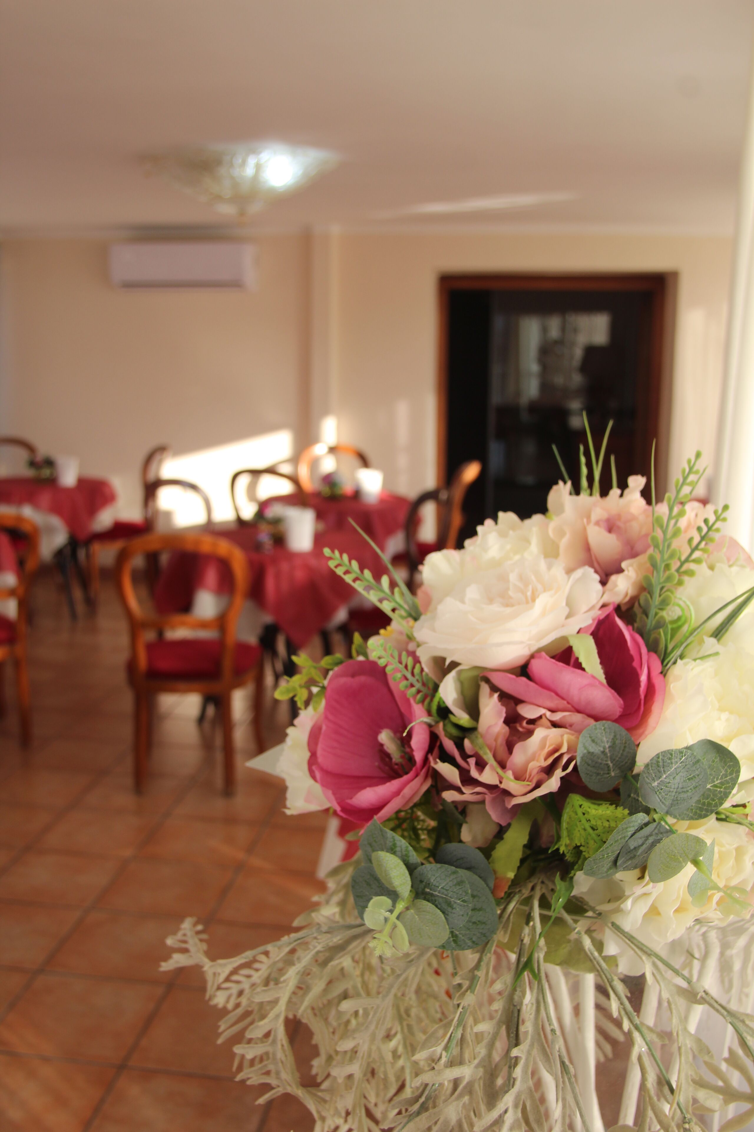 A dining area with tables set for service, chairs, and a floral centerpiece.