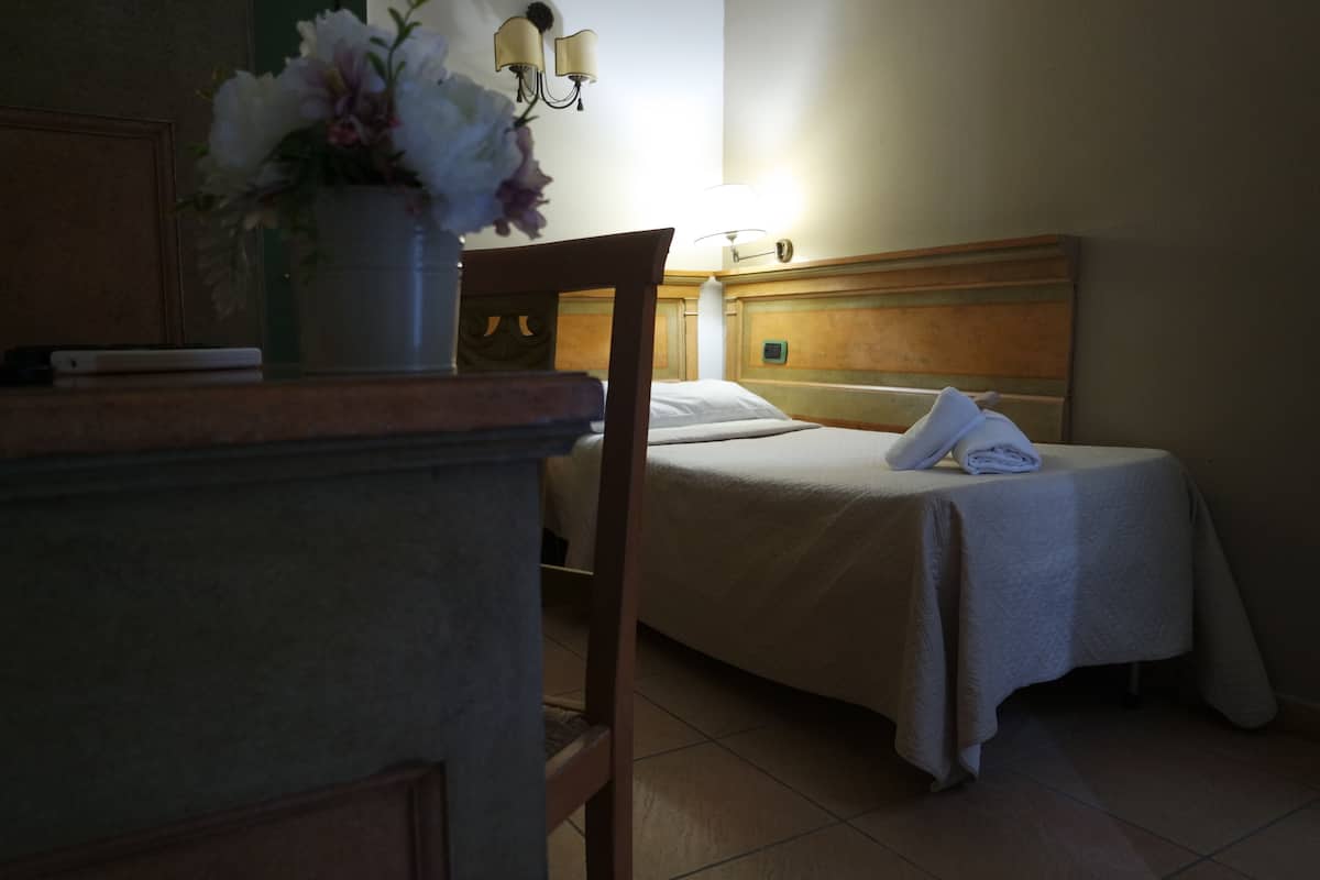Ein Hotelzimmer mit Bett, Nachttisch, Lampe und einer Blumenvase.