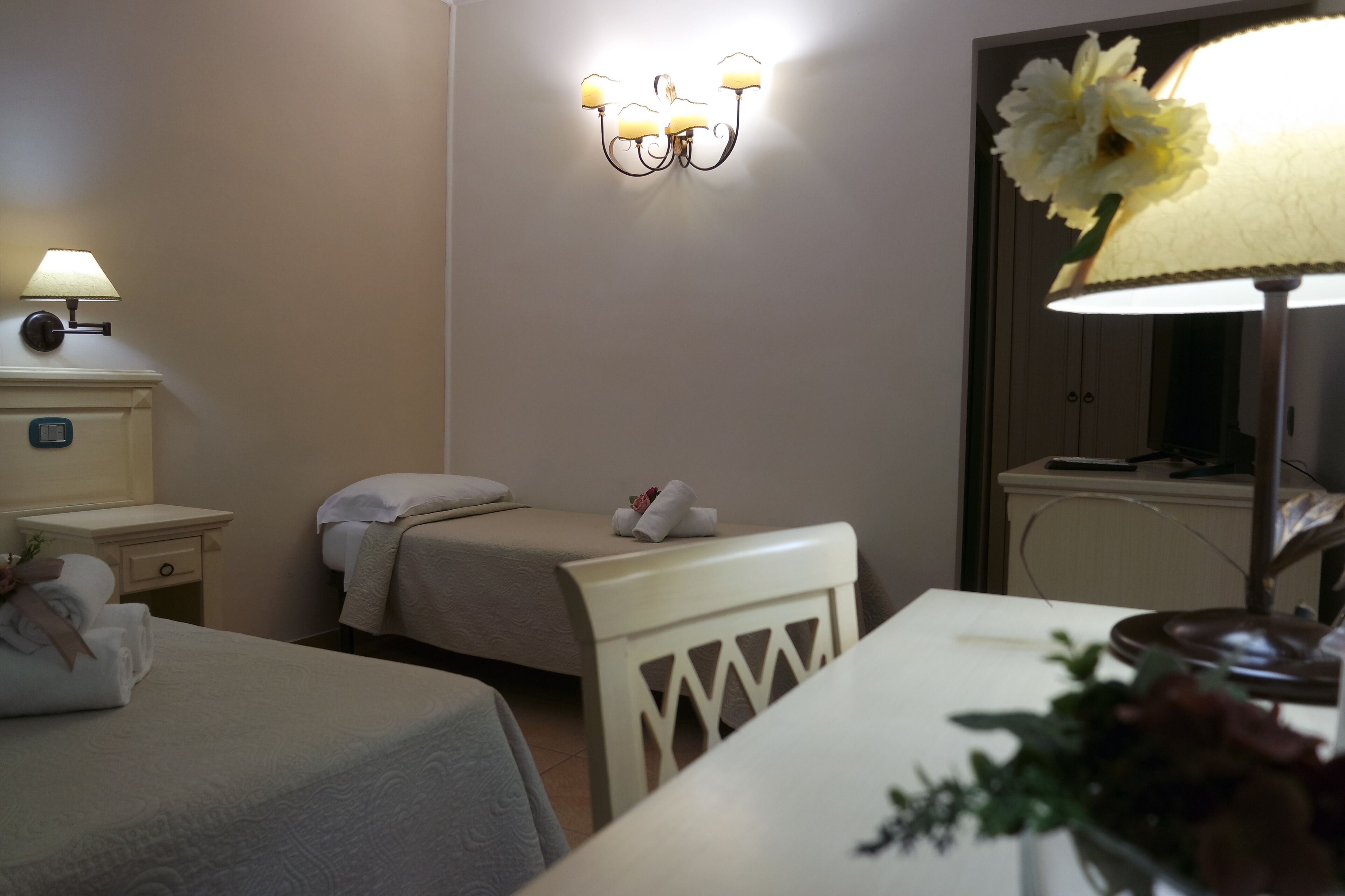 A hotel room with a bed, bedside table, lamp, and a mirror with a flower.