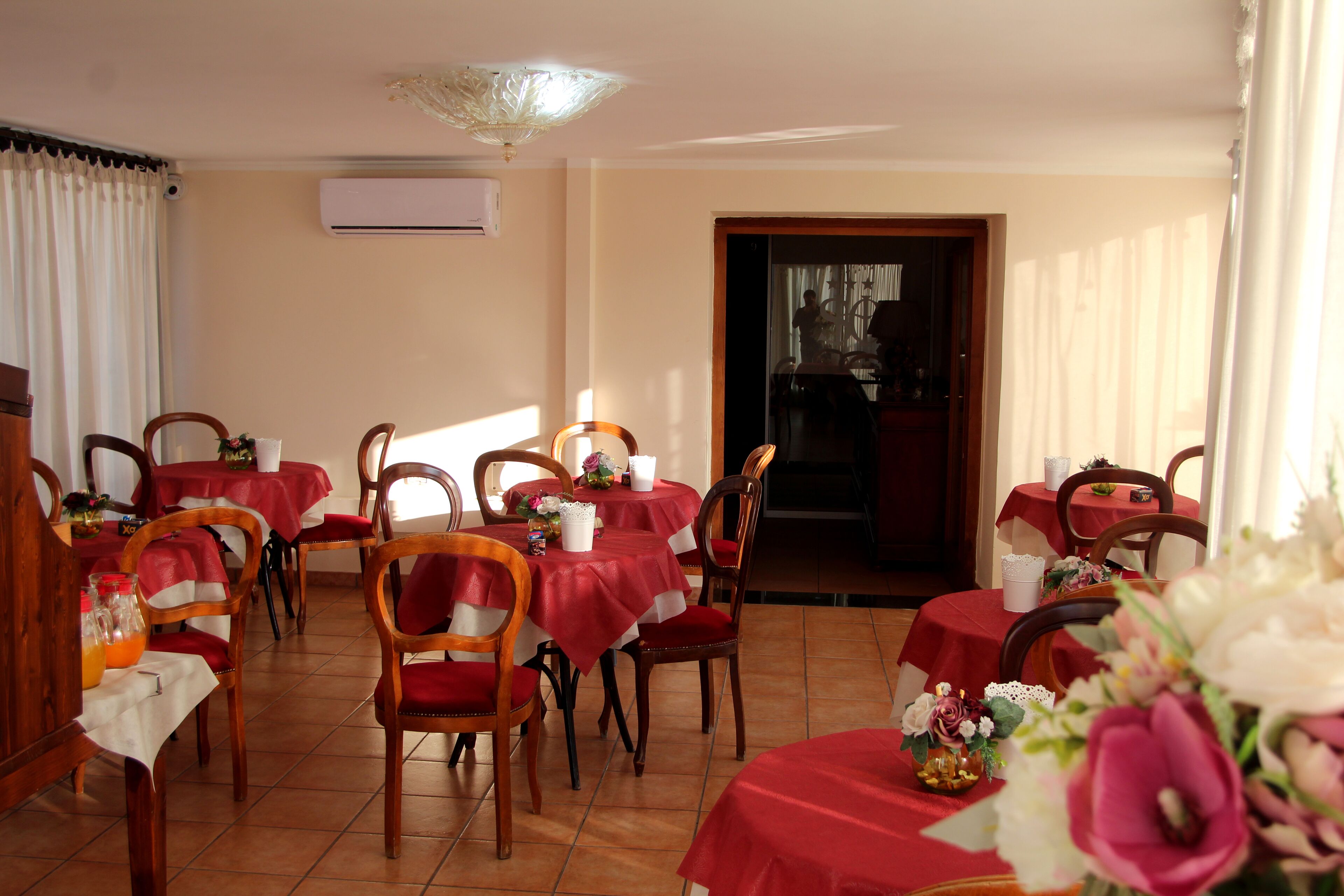 A dining area with multiple tables covered in red tablecloths, wooden chairs, and floral centerpieces.