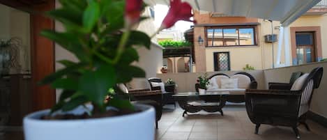 An outdoor patio area with wicker furniture, a white sofa, and a potted plant.